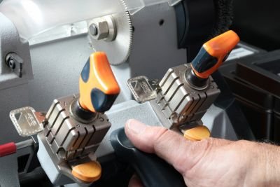 Zwei Schlüsselrohlinge in den Spannbacken einer Fräsmaschine, eine Hand führt den Hebel
